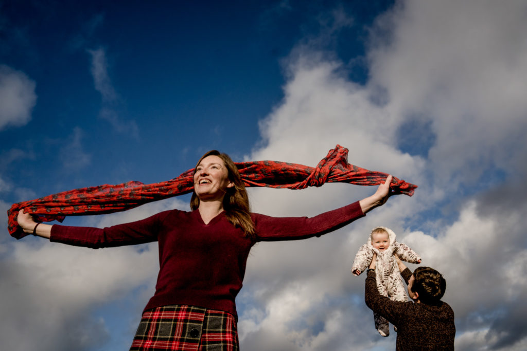woman swinging scarf in foreground whilst the man lifts the baby high in the background  
