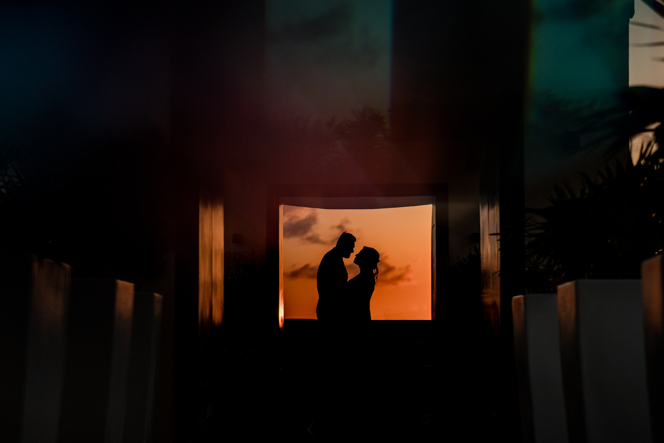 A silhouette photograph of a couple facing each other in a frame infront of a sunset